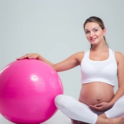 Une femme enceinte en tenue sportive assise sur un tapis de sport, une mains déposée sur sur swisball